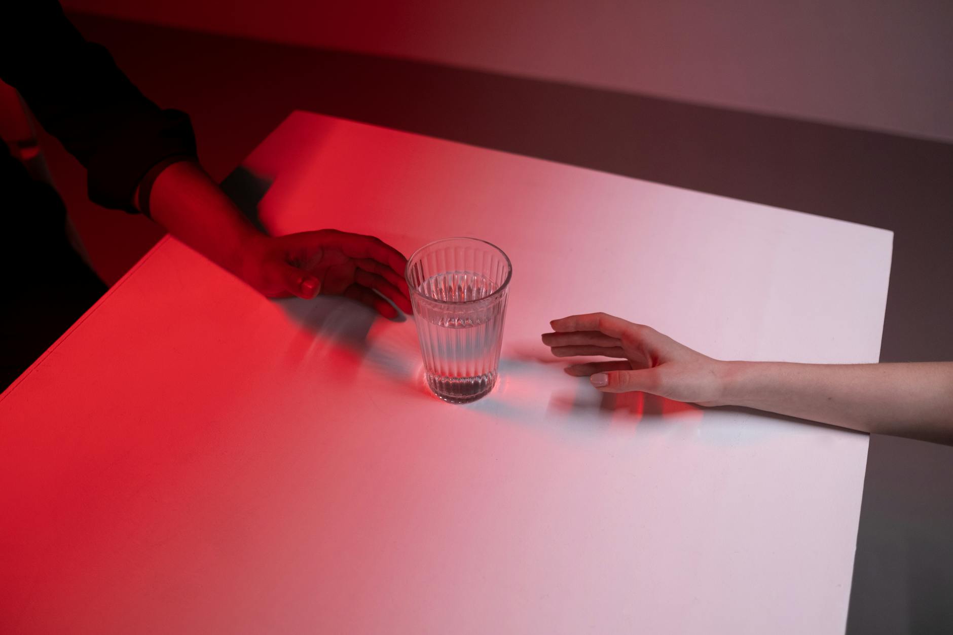 two peoples hands reaching glass of water
