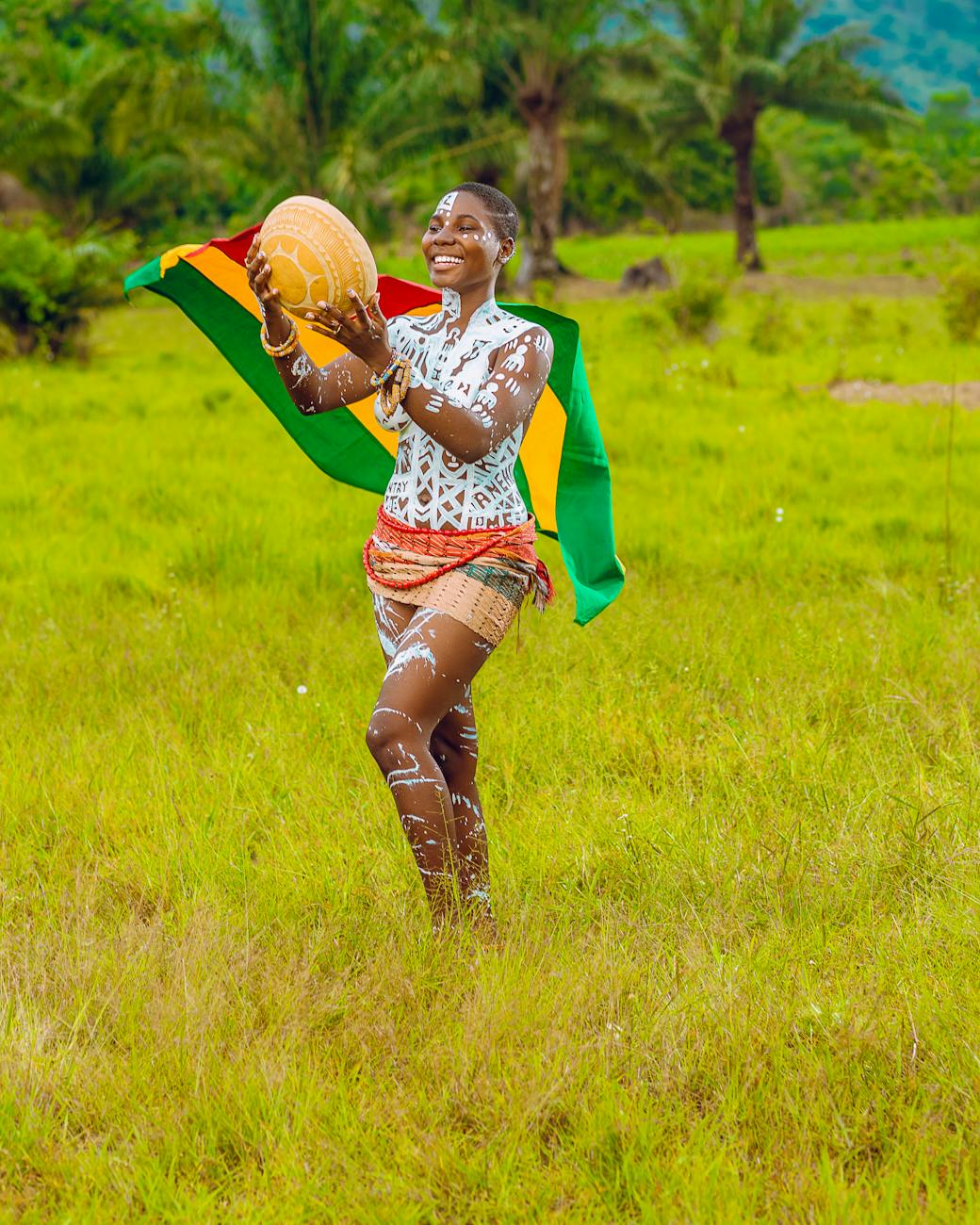 woman with body paint standing on grass field holding a ceramic bowl